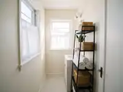 Narrow bathroom with a black metal shelf unit holding rolled towels, rattan baskets, and a snake plant