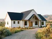 Modern farmhouse with white board-and-batten, black metal roof, black windows and a wood-framed gabled porch