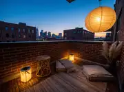 Oversized glowing paper lantern above floor cushions, a rattan stool and solar lanterns on a brick loft balcony
