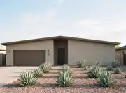 Low-slung greige stucco ranch with a brown garage and front door, bronze sconces and repeating agaves in gravel