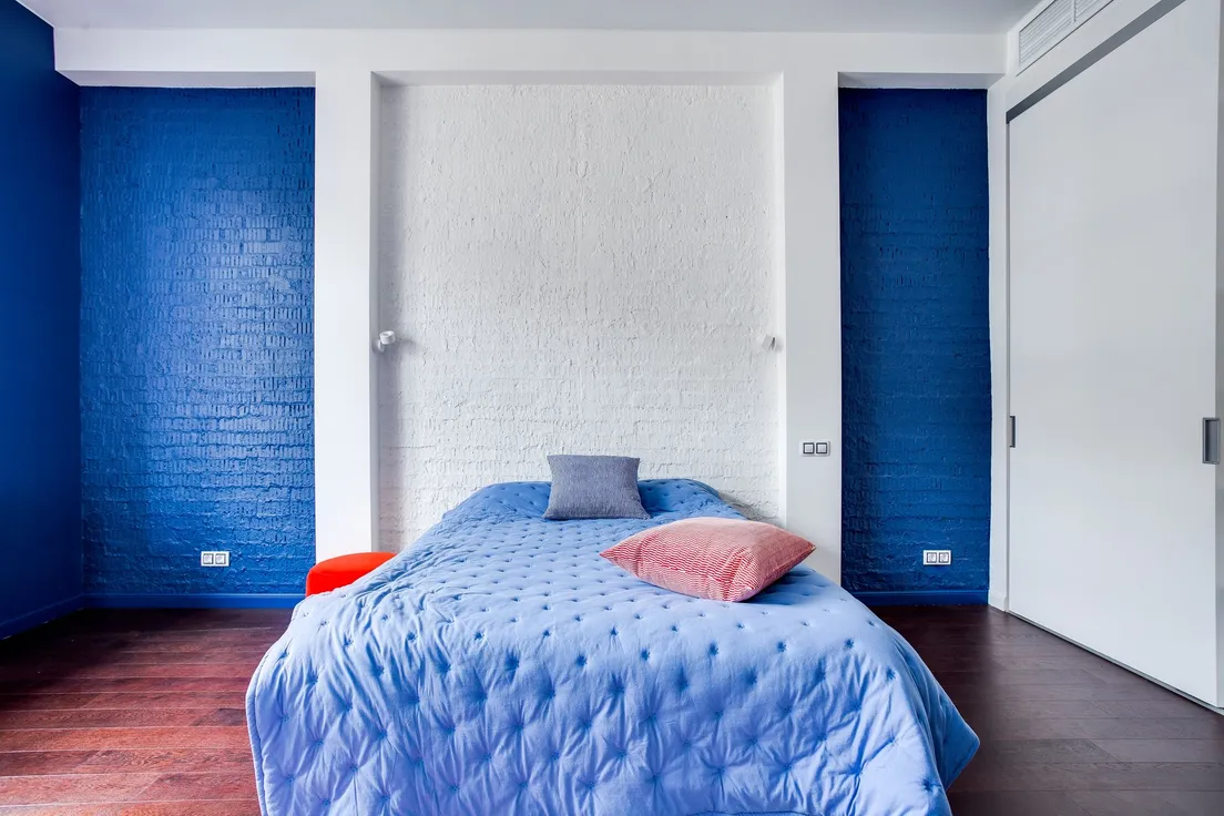 A bedroom with a bold blue accent wall behind a bed with light blue bedding