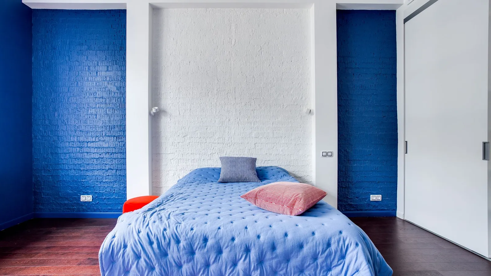 A bedroom with a bold blue accent wall behind a bed with light blue bedding