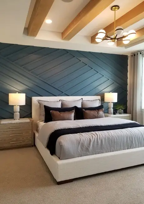 A bedroom with a bold blue accent wall behind the bed and neutral walls elsewhere, an example of an accent wall as a bedroom paint color idea