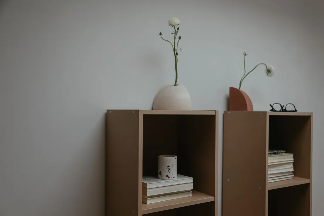 A minimalist bookshelf styled with a ceramic vase, dried flowers, and a small stack of books