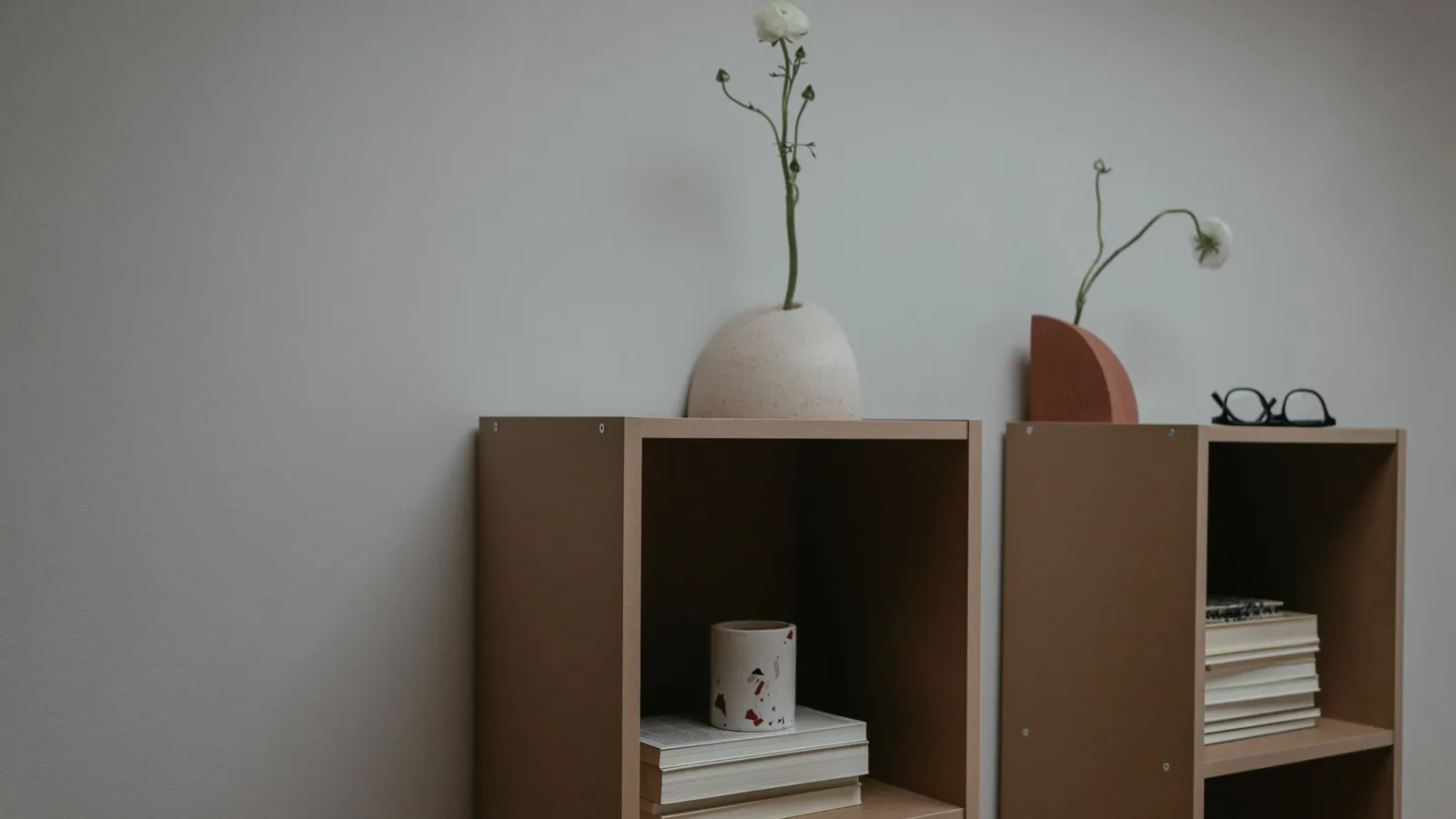 A minimalist bookshelf styled with a ceramic vase, dried flowers, and a small stack of books