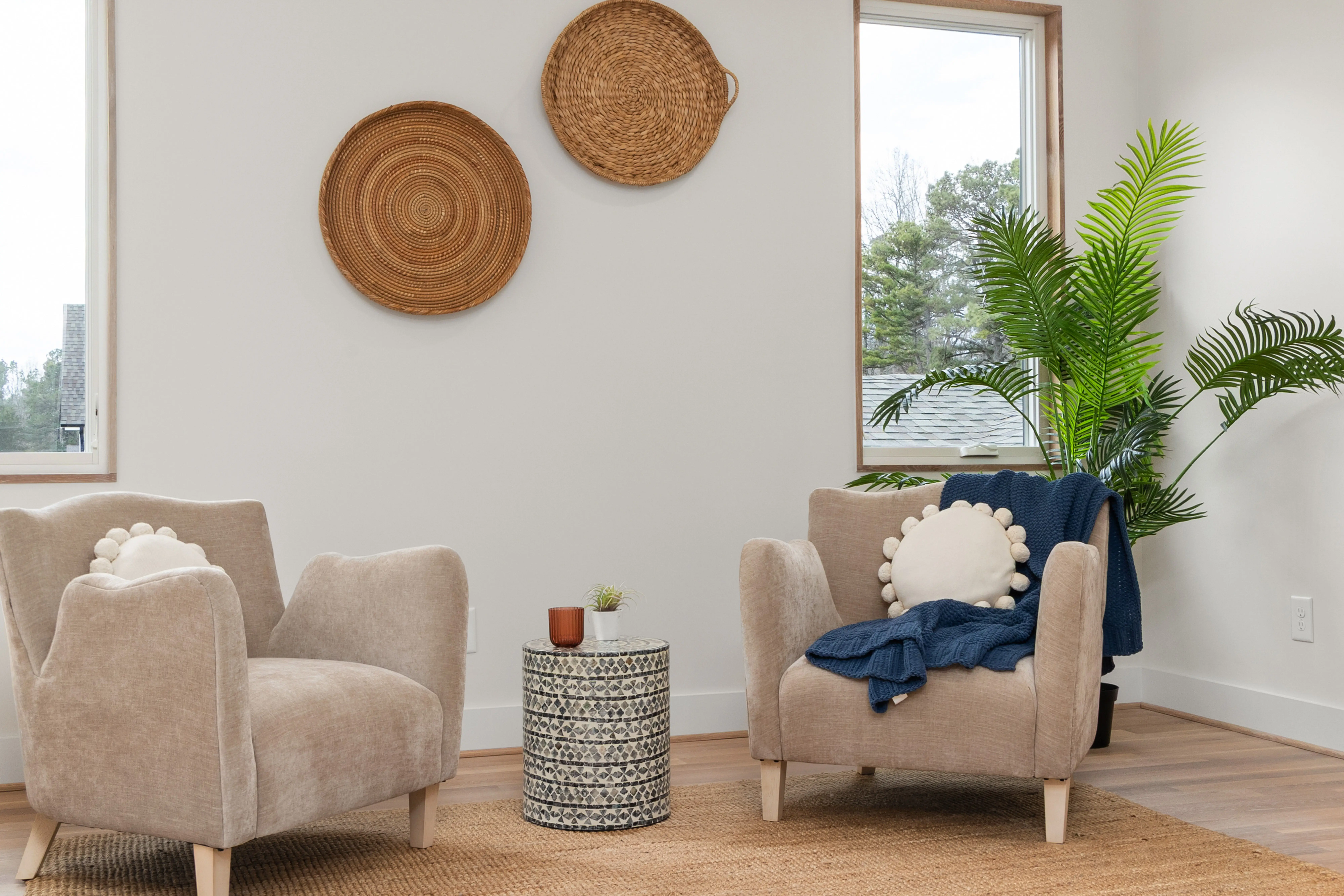 Two mismatched beige accent chairs with woven wall decor in a minimalist living room