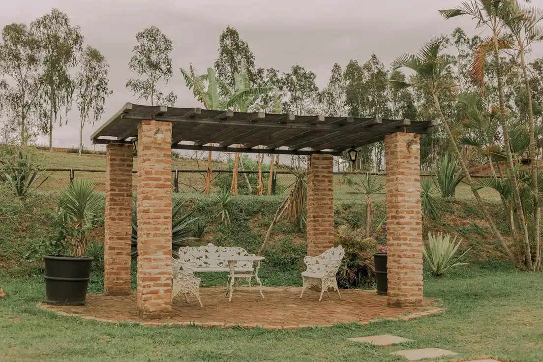 A freestanding patio cover with brick posts and a slatted wood roof over a garden seating area
