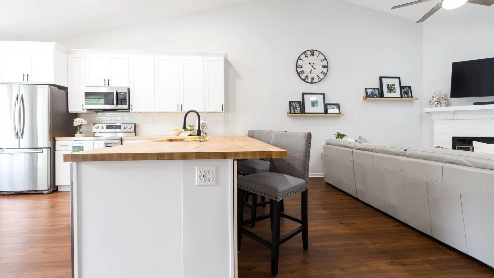 Two wooden counter stools tucked under a butcher block kitchen counter facing a small living room