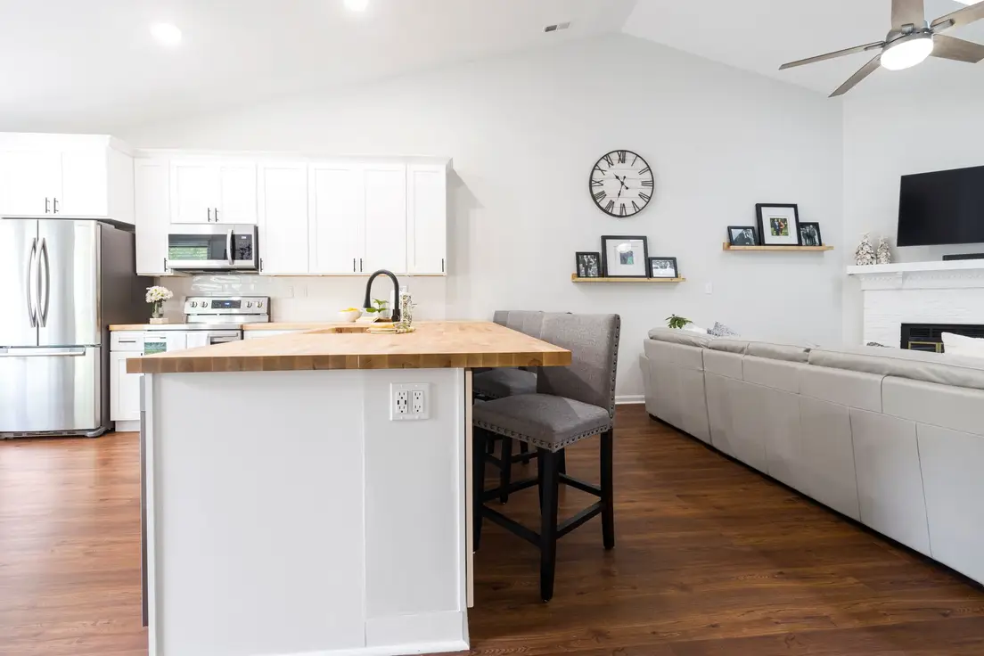 Two wooden counter stools tucked under a butcher block kitchen counter facing a small living room