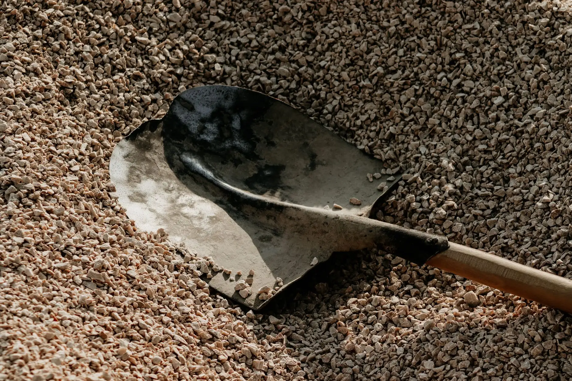 A shovel resting in a pile of compacted crushed stone base for a patio