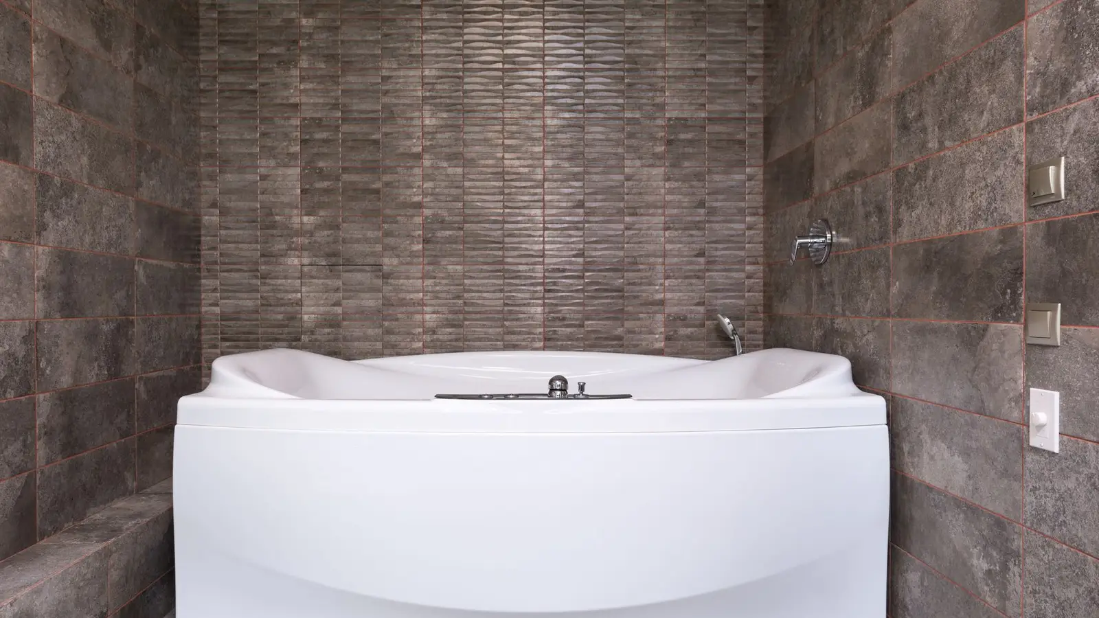 A white bathtub with a small bathroom tile surround in a neutral pattern