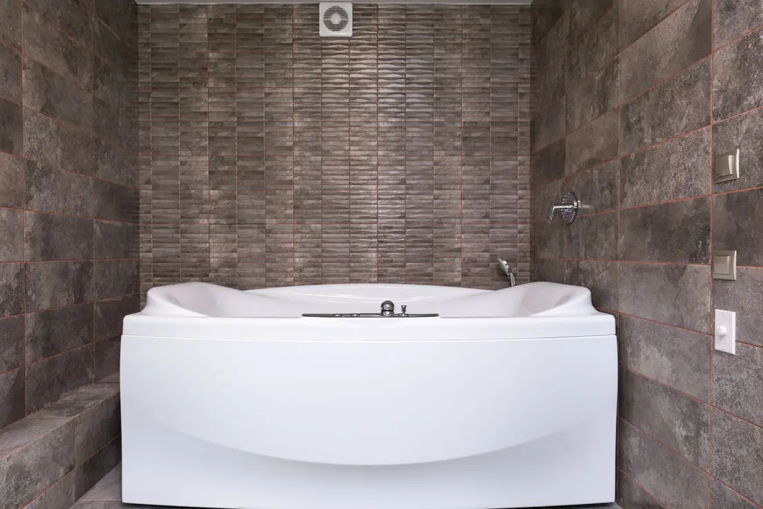 A white bathtub with a small bathroom tile surround in a neutral pattern