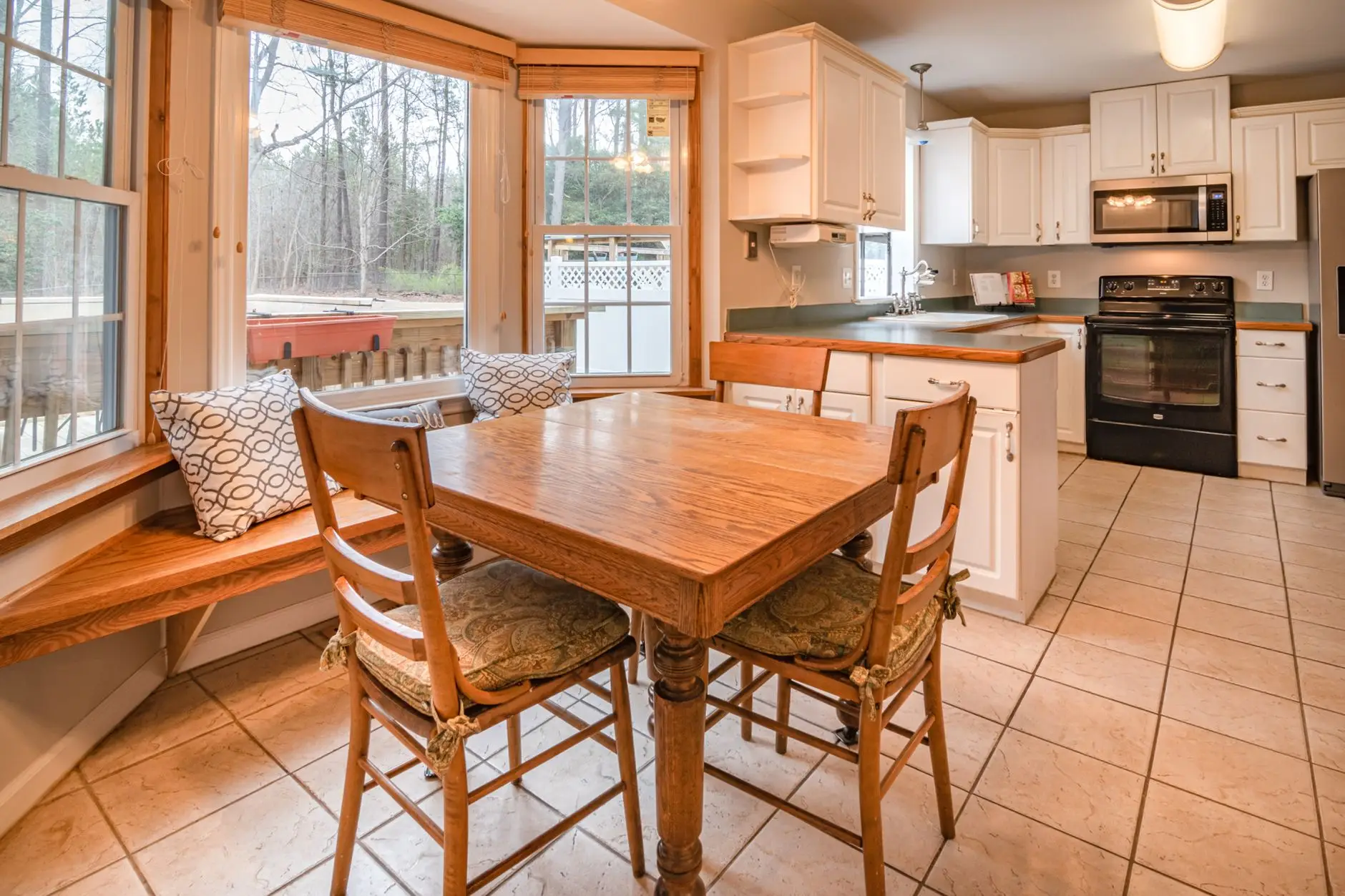 A builder-grade oak table and bench seat tucked into a bay window breakfast nook