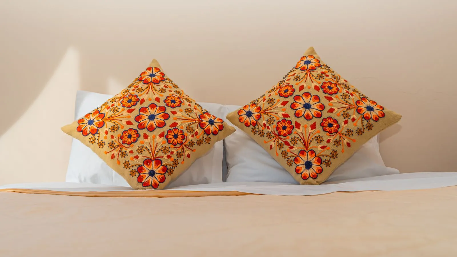 Two mismatched orange-and-blue embroidered floral throw pillows layered on a bed