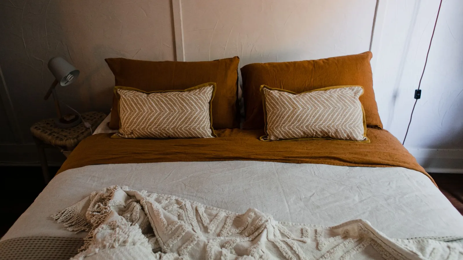 A bed layered with mustard bedding, two textured throw pillows, and a woven cream blanket