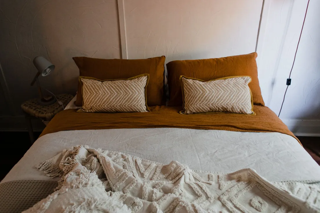 A bed layered with mustard bedding, two textured throw pillows, and a woven cream blanket