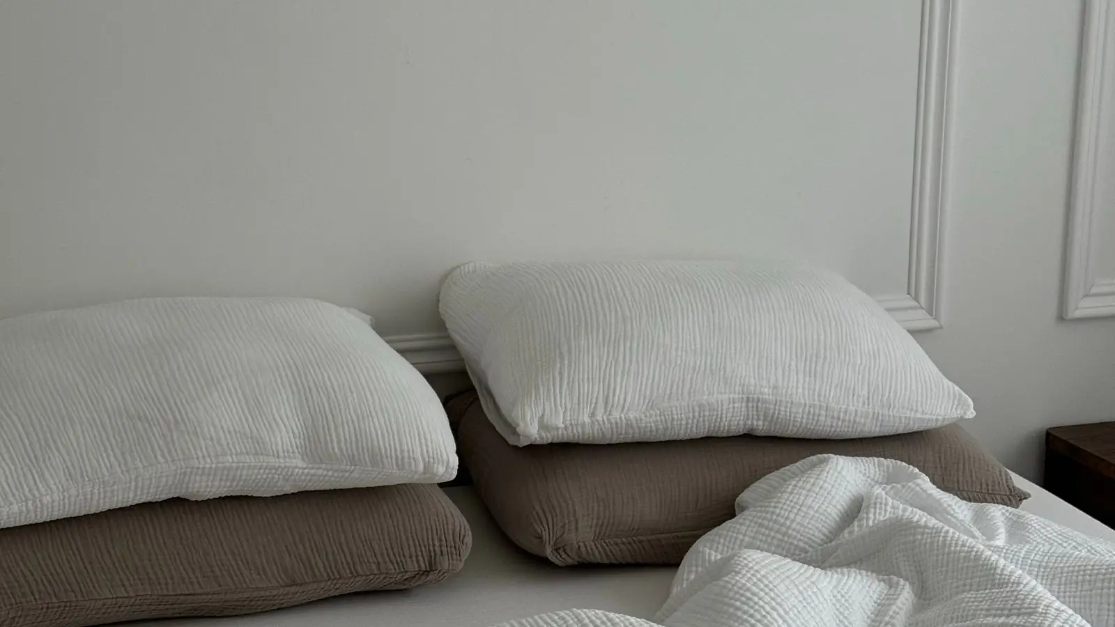 Layered white and taupe muslin bedding on an unmade bed