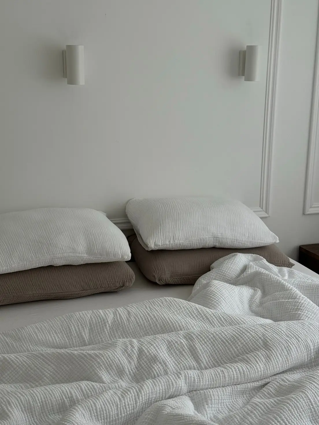 Layered white and taupe muslin bedding on an unmade bed