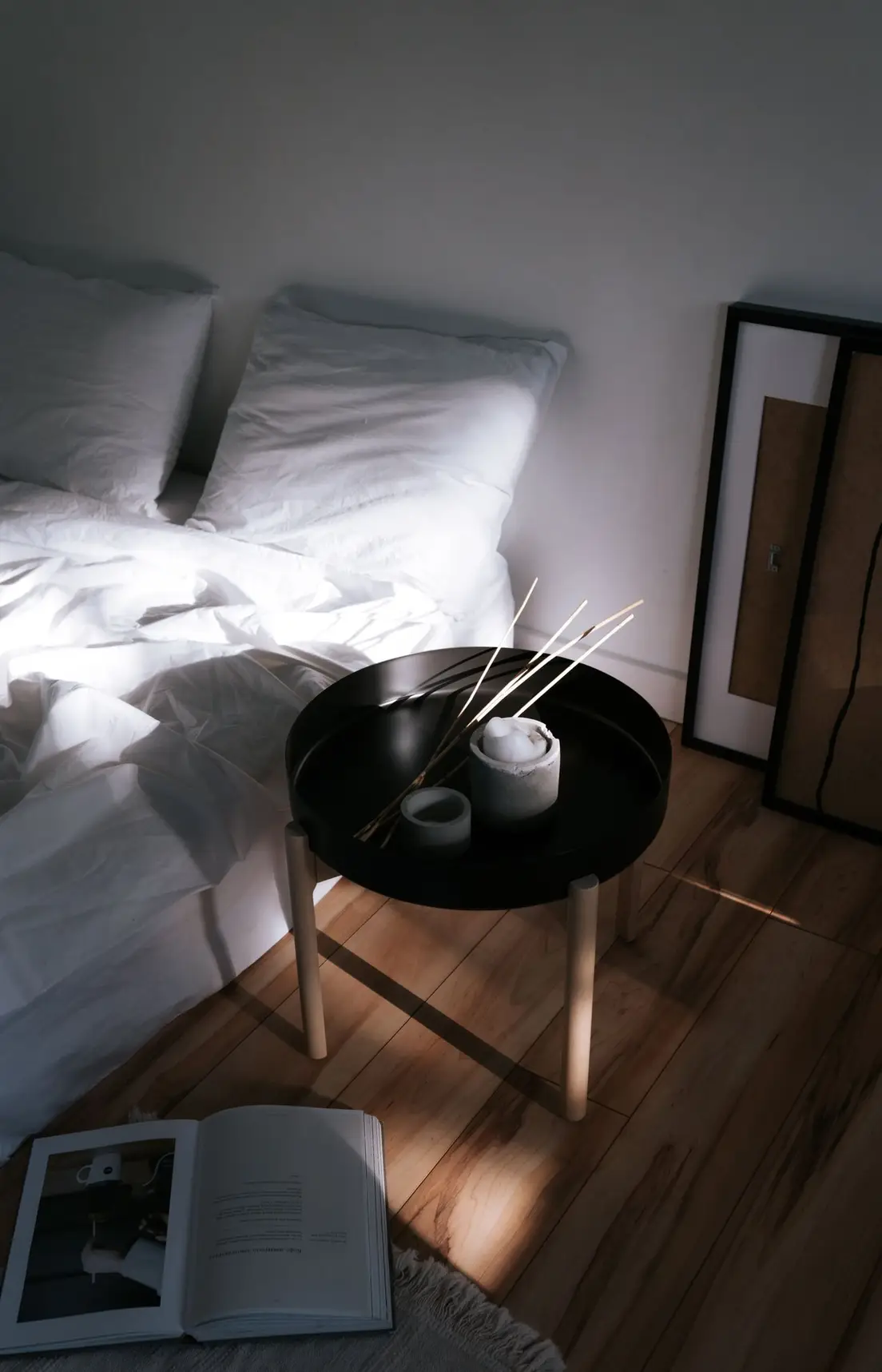 A serene japandi bedroom with white linen bedding, a round wood side table, and dried branches in a vase
