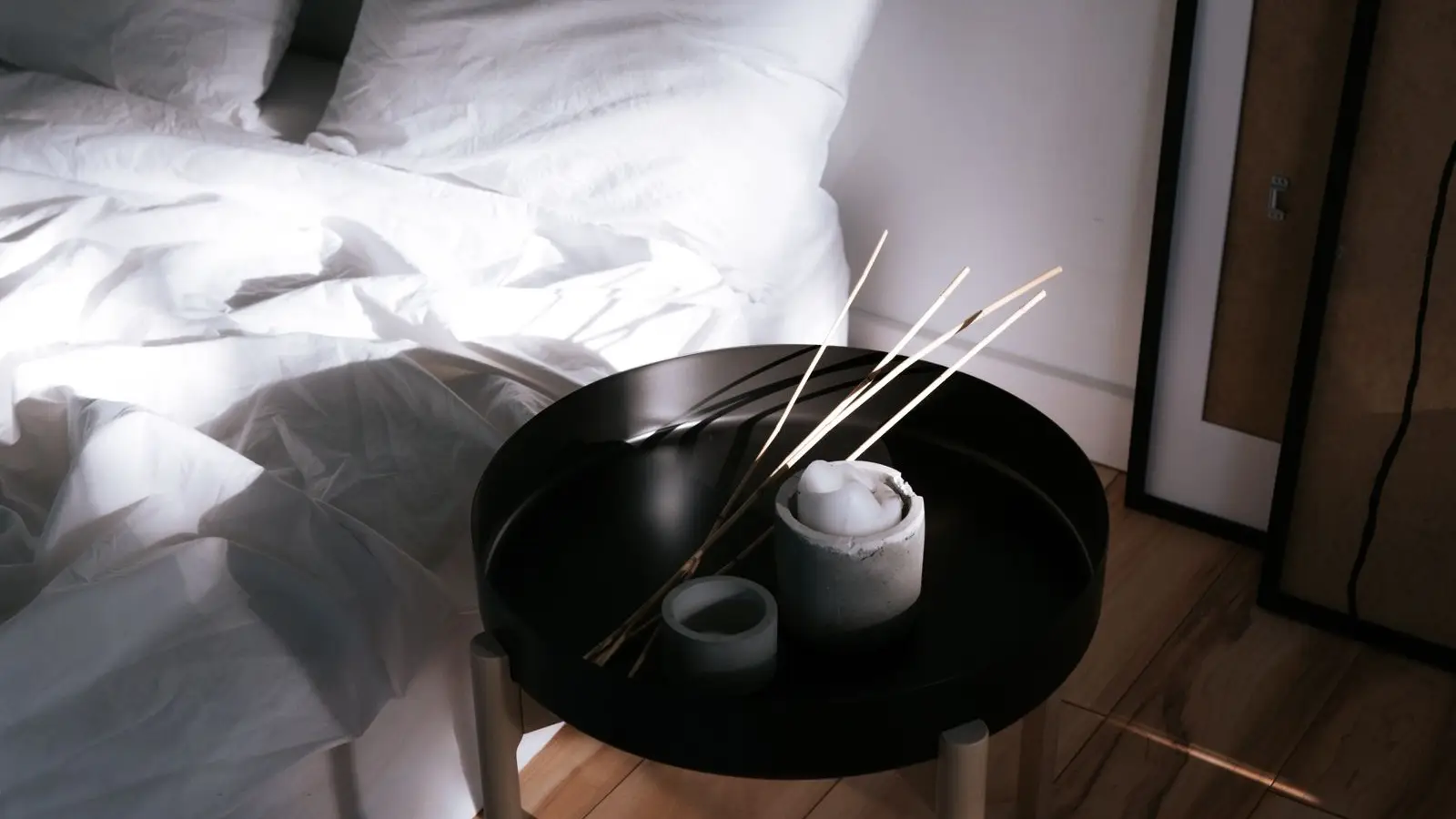 A serene japandi bedroom with white linen bedding, a round wood side table, and dried branches in a vase