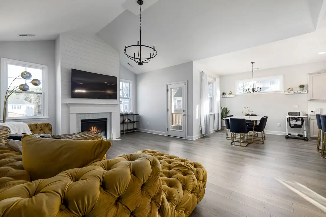 A black iron candle-style chandelier hanging from a vaulted ceiling in a modern farmhouse living room with a white shiplap fireplace wall