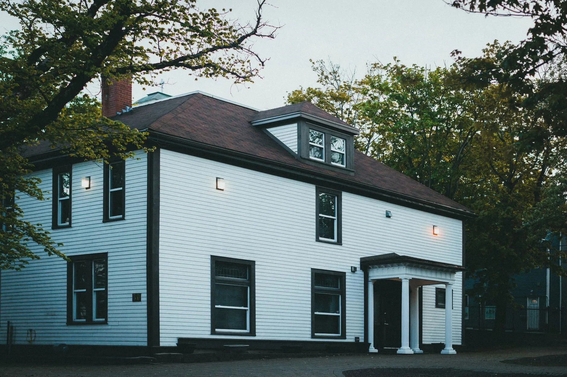 A white modern farmhouse exterior with black-trimmed windows lit at dusk