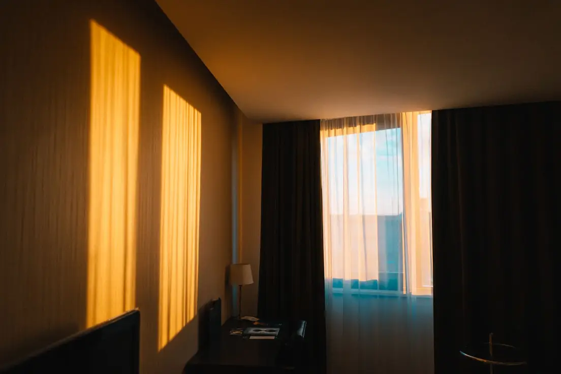 Dark blackout curtains in a bedroom with morning light leaking around the edges of the window