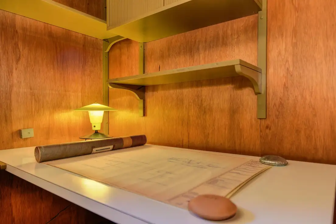 Rolled blueprints and a vintage lamp on a desk against wood paneling, planning a mid-century ranch renovation budget