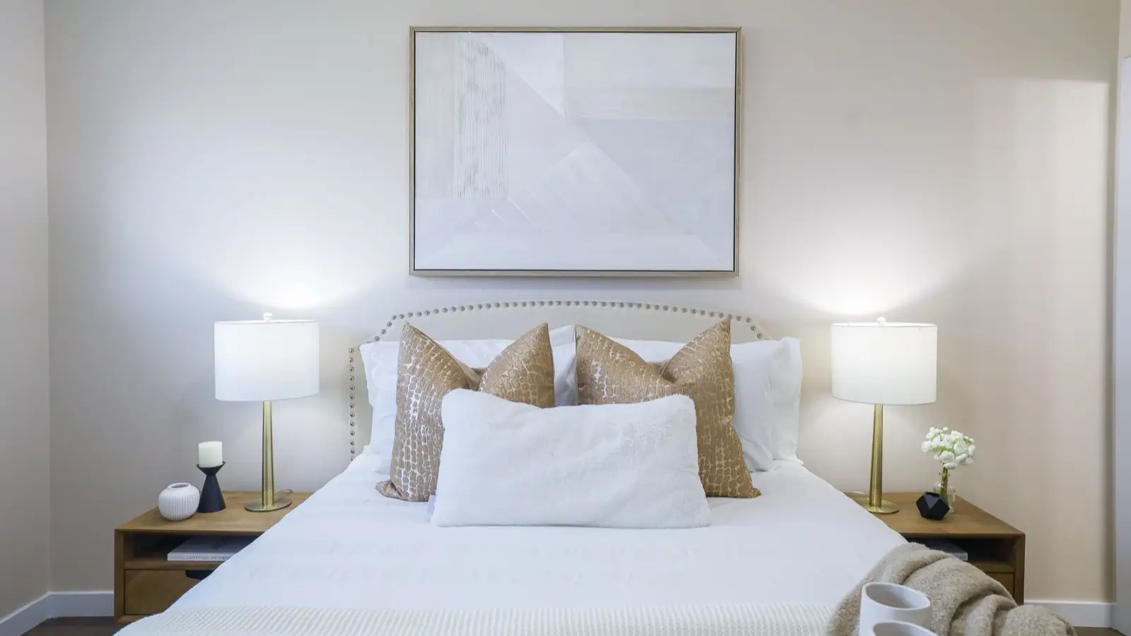 A neutral and gold bedroom palette with a nailhead headboard, warm pillows, and matching lamps