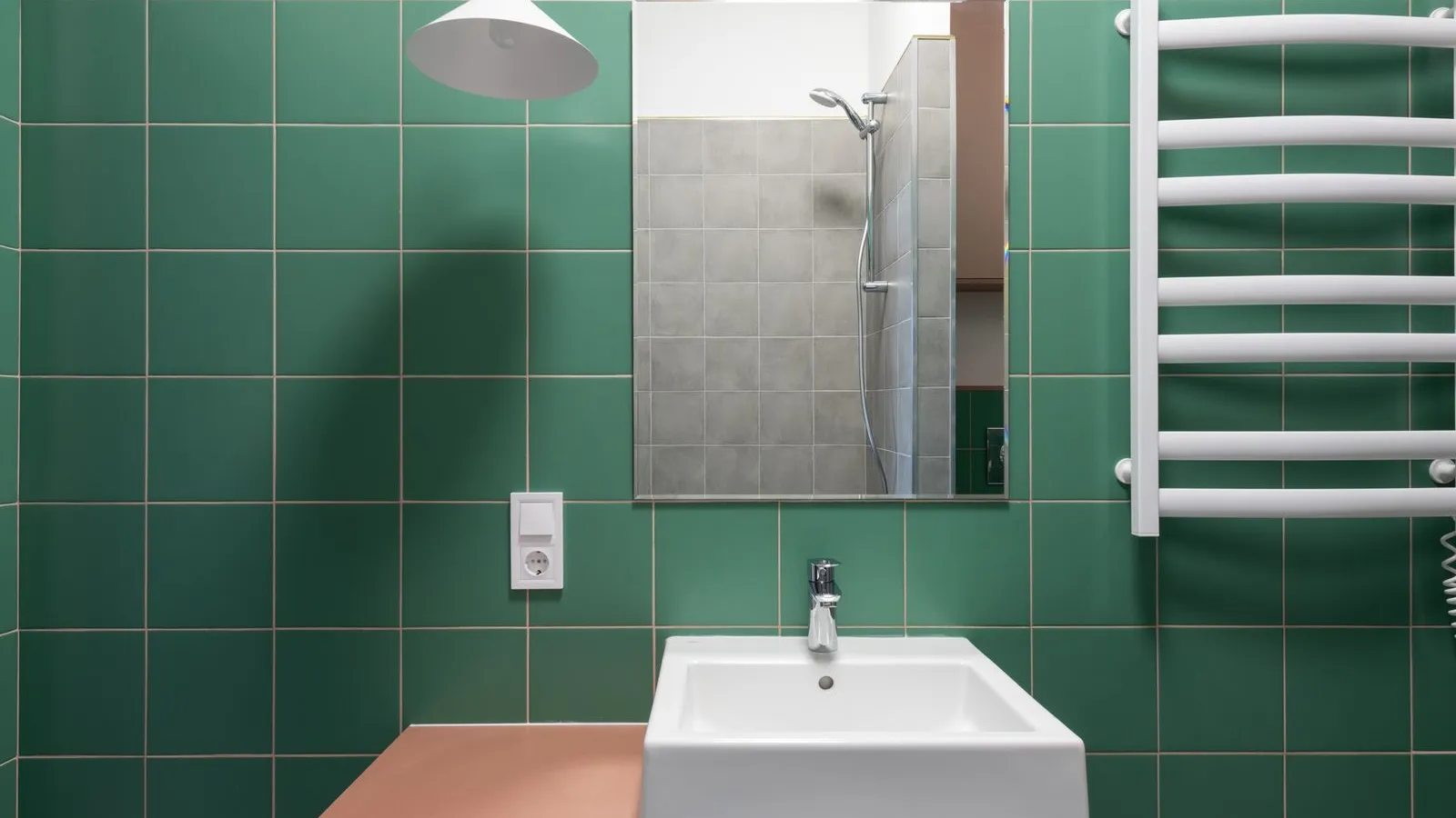 A powder room with deep green tile walls, a terracotta vanity, and a pendant light
