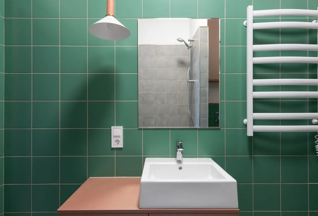 A powder room with deep green tile walls, a terracotta vanity, and a pendant light