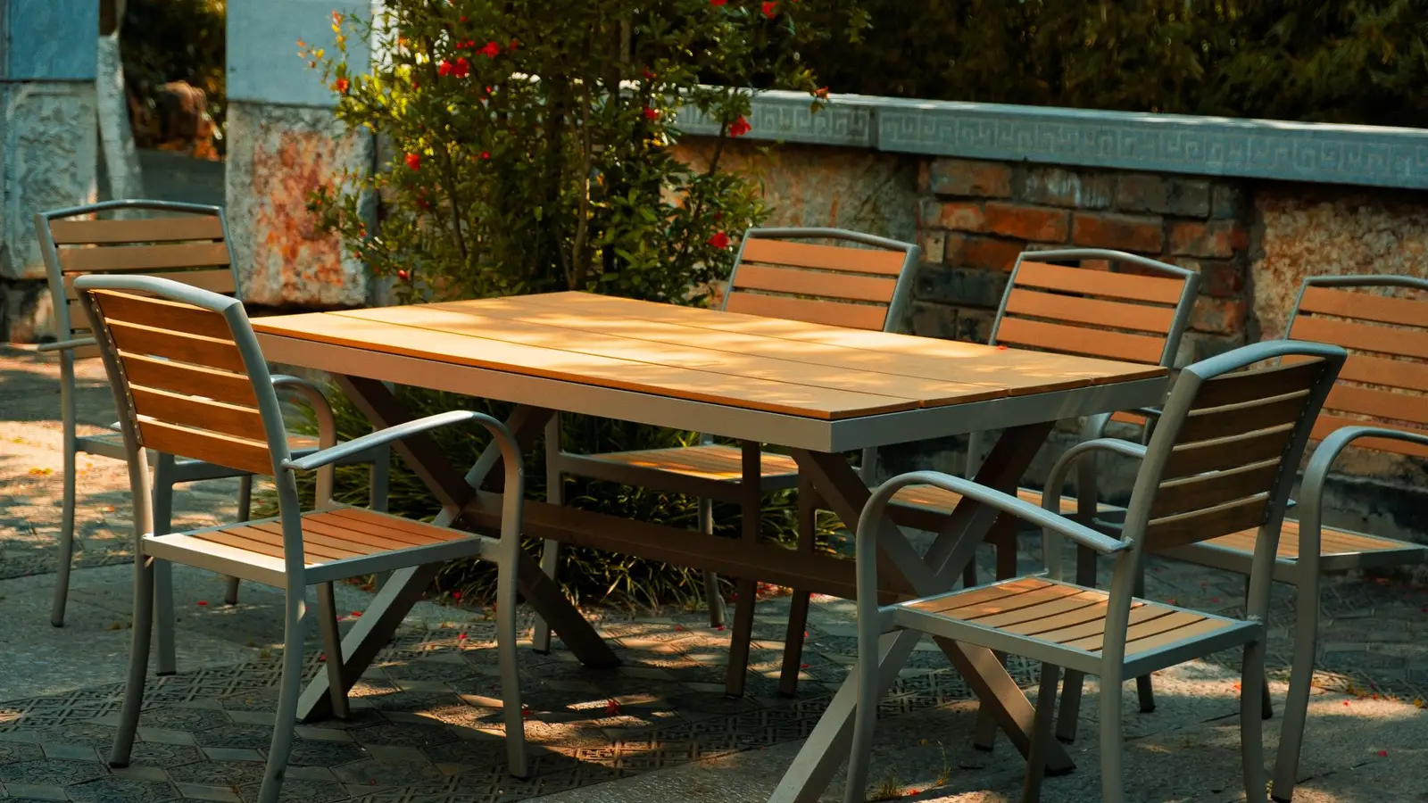Outdoor dining set on a patterned paver patio framed by a low stone wall