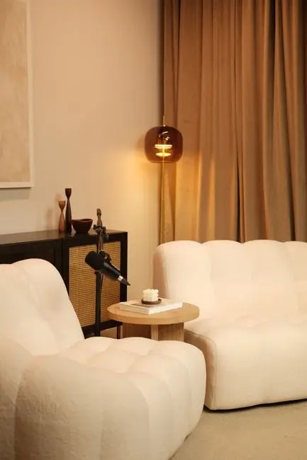 A cream bouclé sofa and matching armchair in an organic modern living room with warm curtains