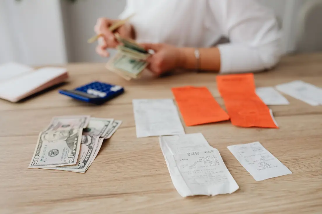 Cash, receipts, and a calculator laid out on a wooden table while someone tallies a home decor budget