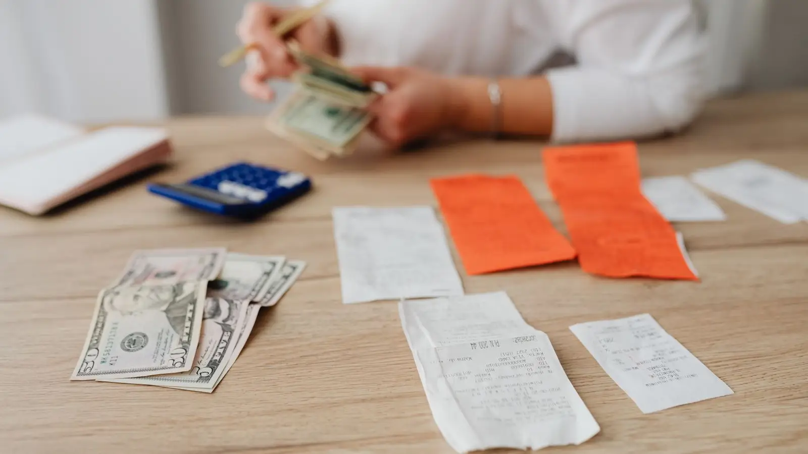 Cash, receipts, and a calculator laid out on a wooden table while someone tallies a home decor budget