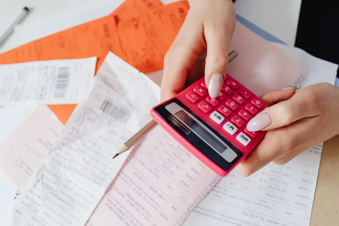 A person using a calculator with receipts to add up a home exterior budget