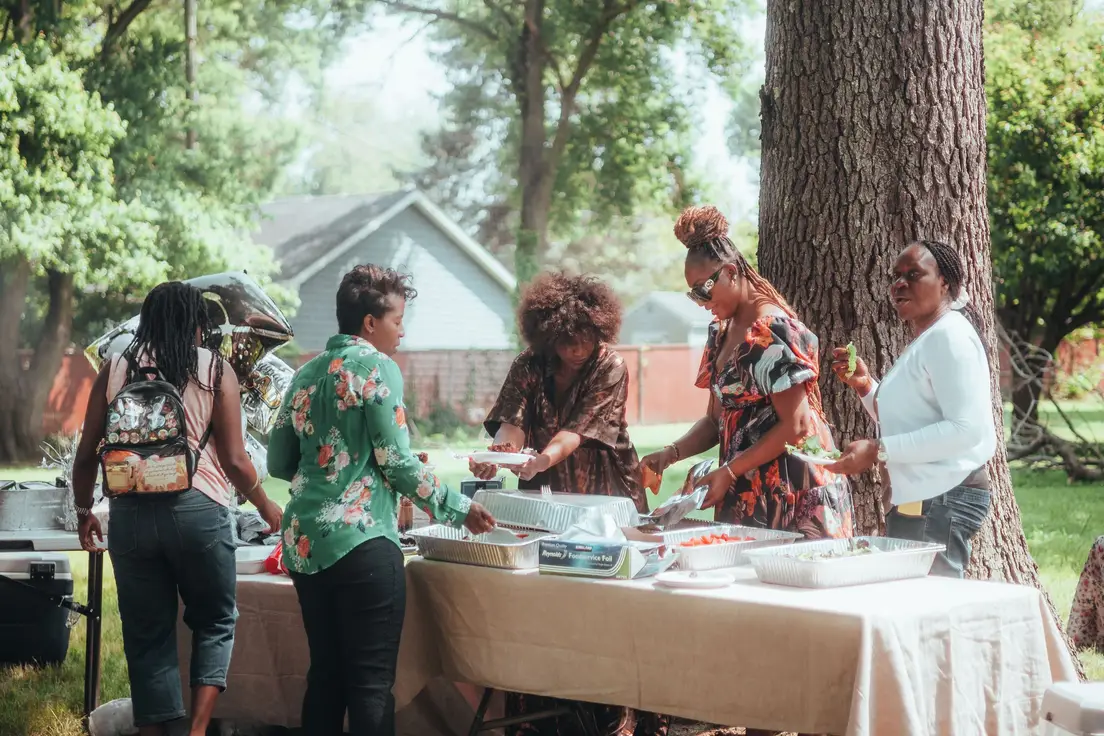 Guests serving themselves buffet-style at an outdoor backyard party table