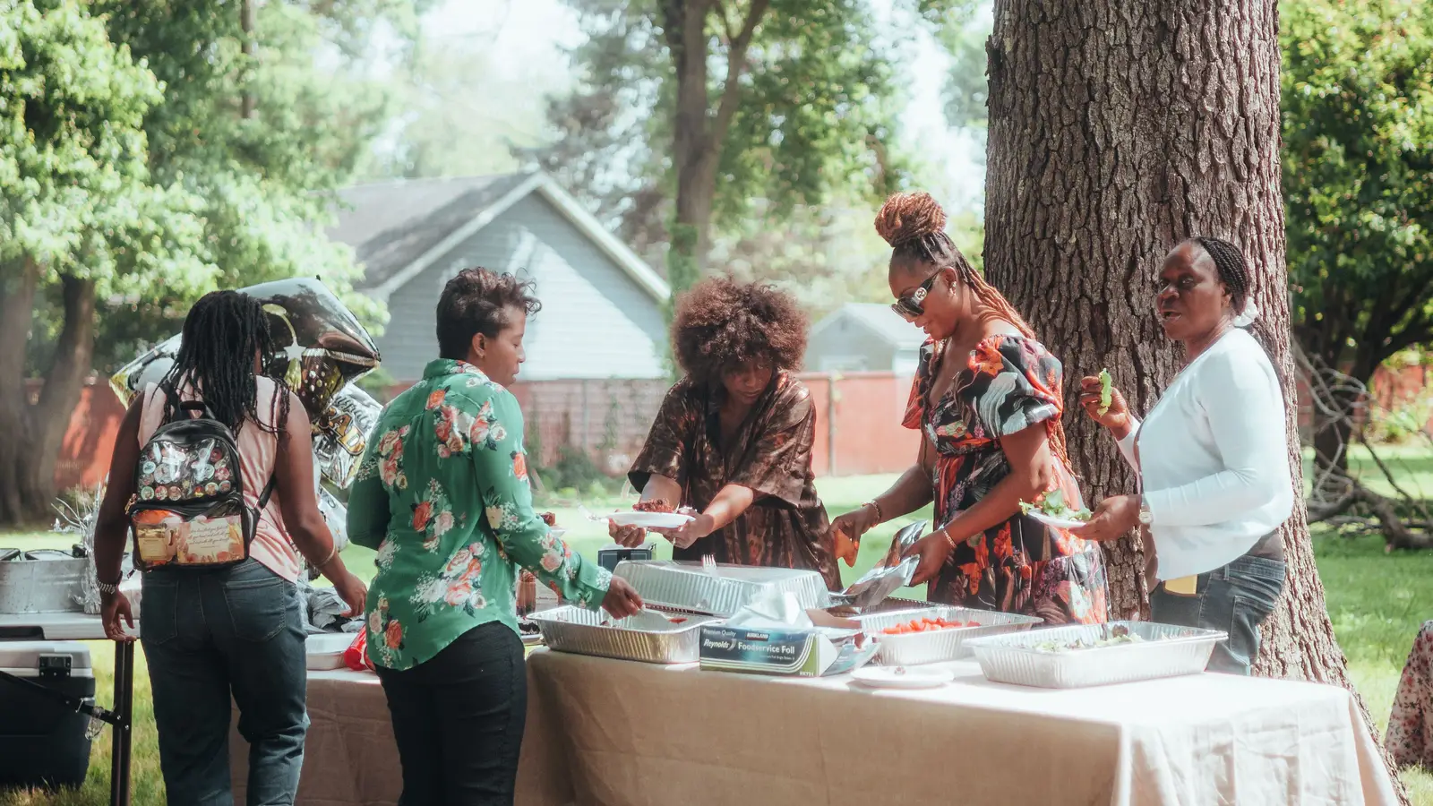 Guests serving themselves buffet-style at an outdoor backyard party table
