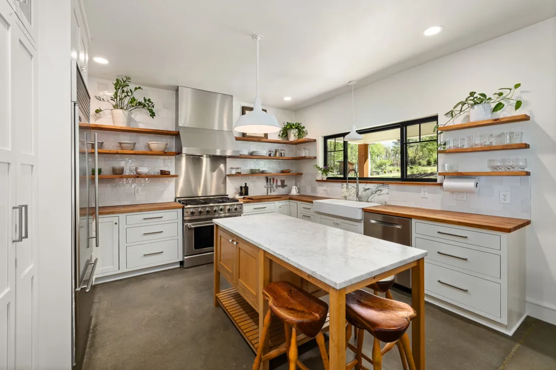 A modern farmhouse kitchen island with a light butcher block-style countertop and wood barstools