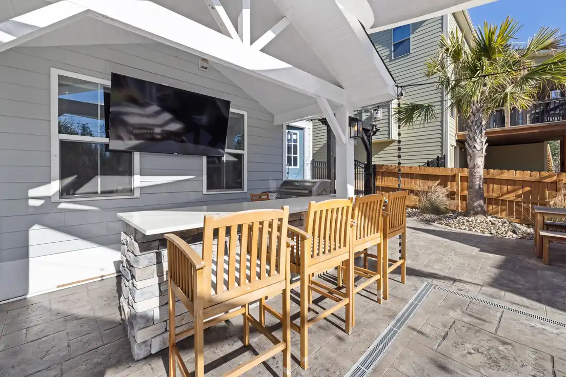 A large gable patio cover over an outdoor kitchen bar with a mounted TV and wood barstools