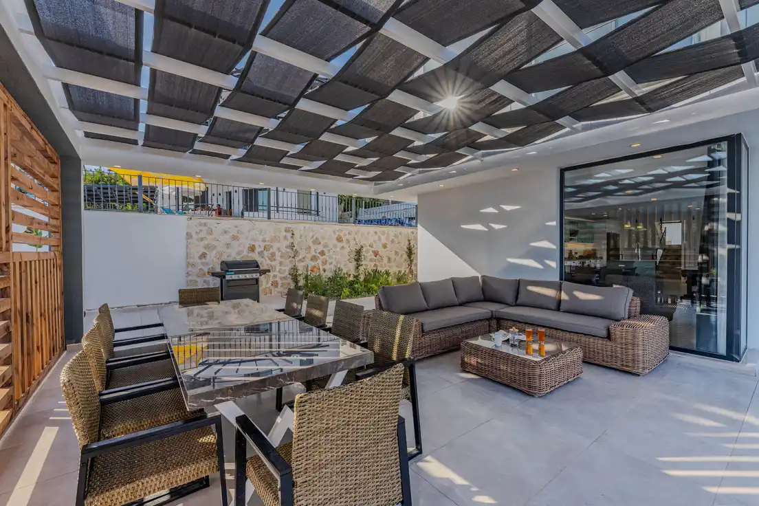 A white pergola-style patio cover with fabric shade strips over an outdoor dining and lounge area