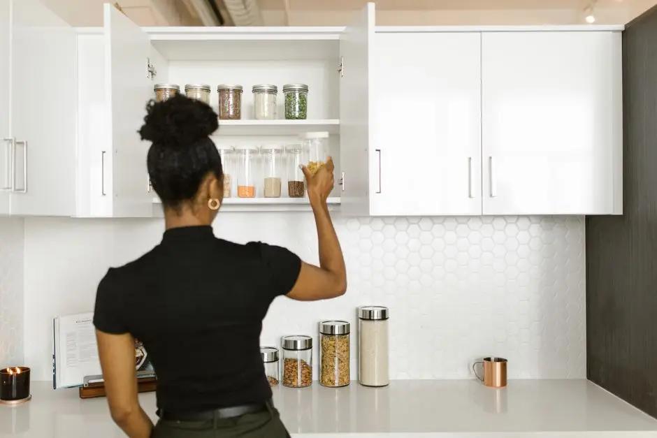 A woman organizing labeled jars inside an open kitchen cabinet in a small apartment