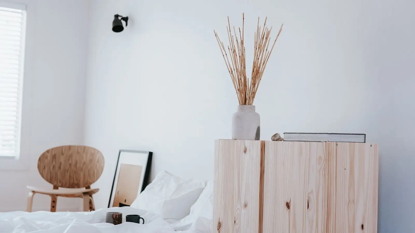 A minimalist bedroom corner with a wood cabinet, a folded pillow, and a plain wall