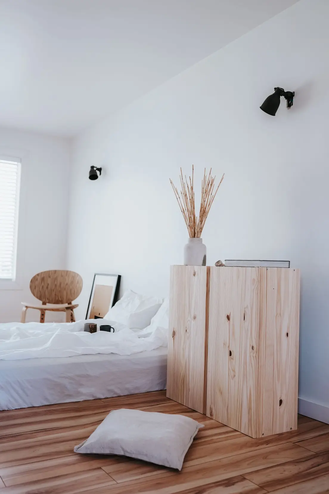 A minimalist bedroom corner with a wood cabinet, a folded pillow, and a plain wall