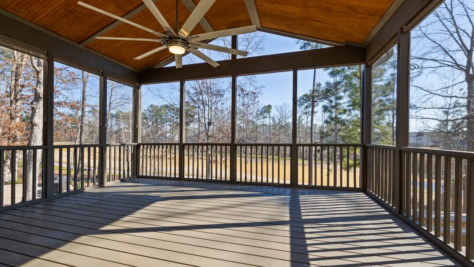 A large wood ceiling fan mounted on the vaulted wood ceiling of a screened patio