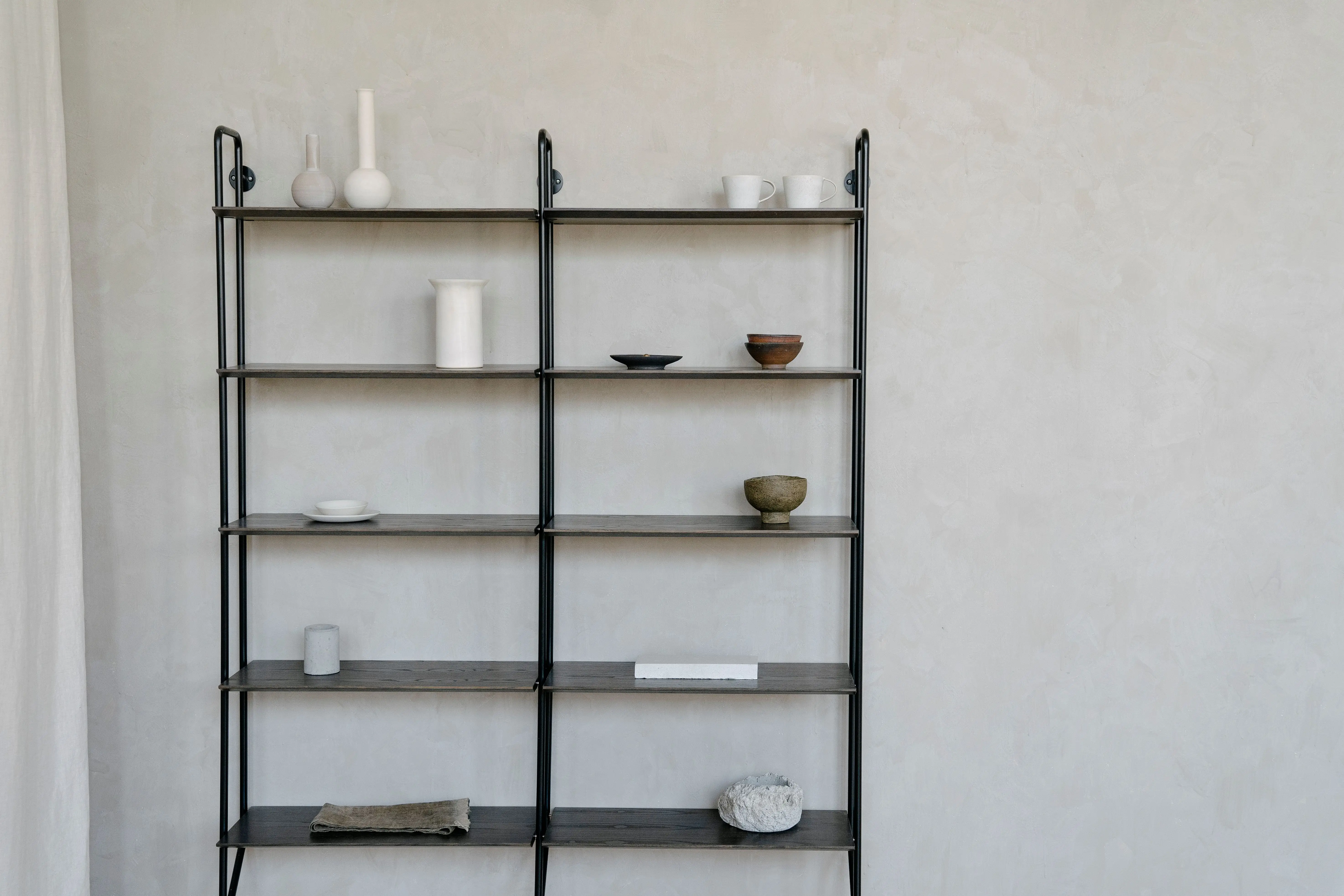 Minimalist shelving styled with a few ceramic pieces and pottery against a plain wall