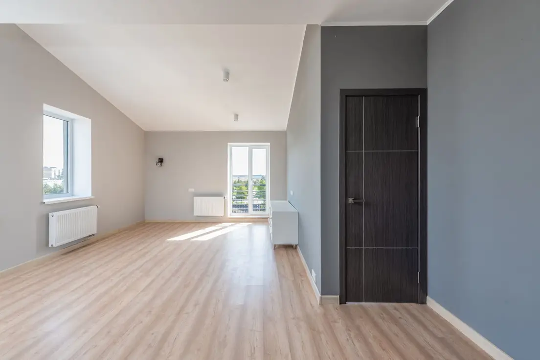 An empty apartment room with wood flooring and a dark interior door, the kind of open floor plan a temporary wall would divide
