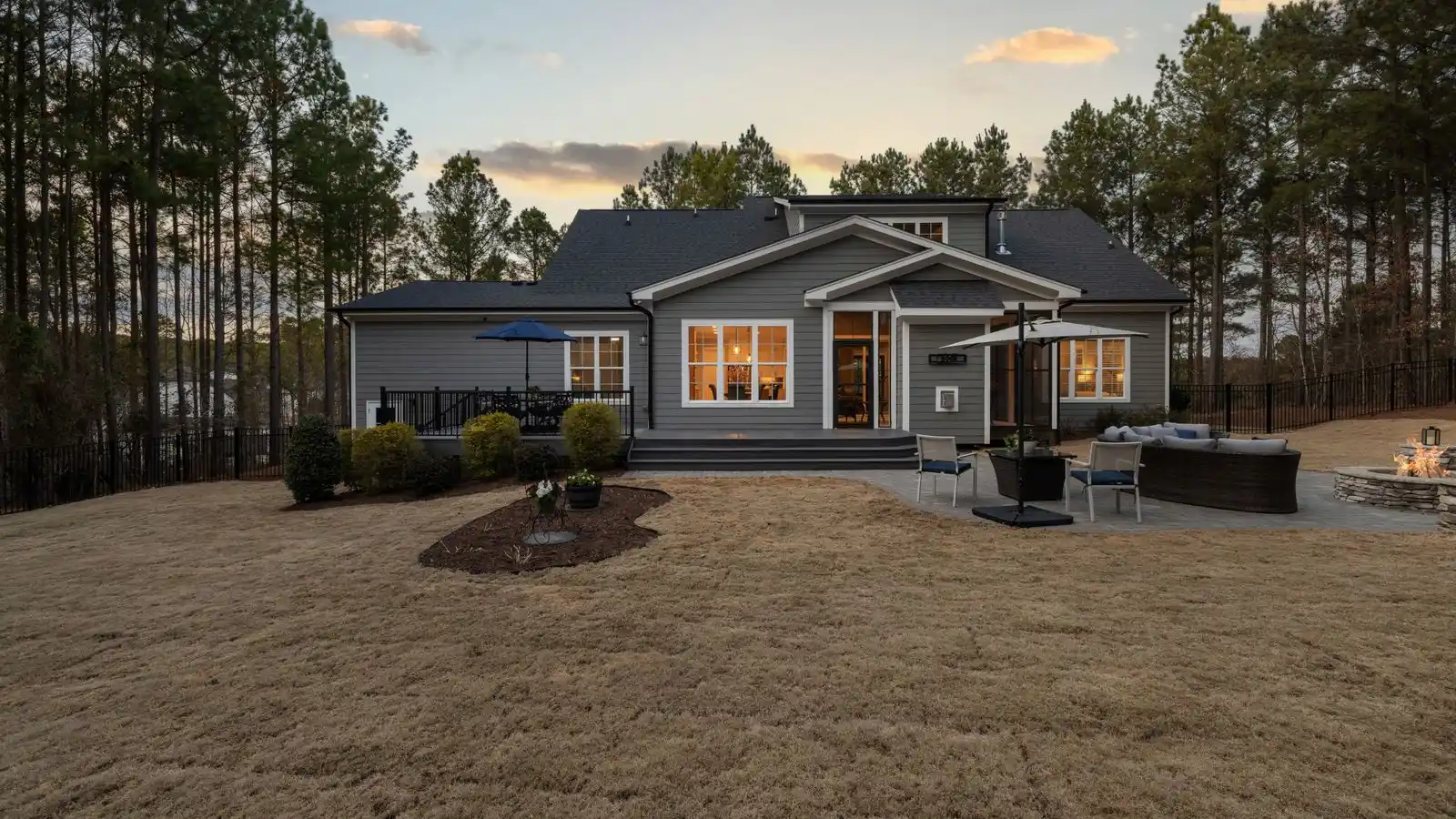 A suburban house with a large lawn and a fire pit seating area set at the far corner of the yard