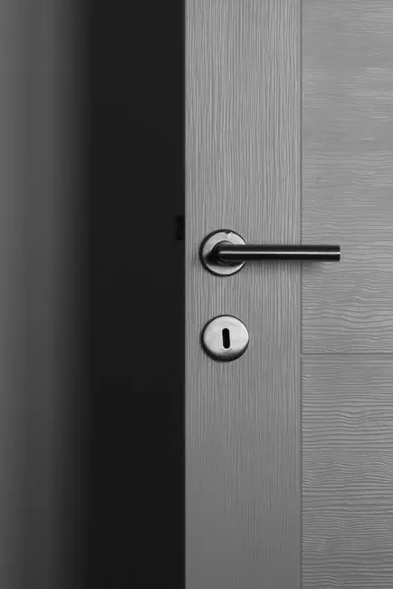 A close-up of a modern black lever door handle on a grey wood-grain door