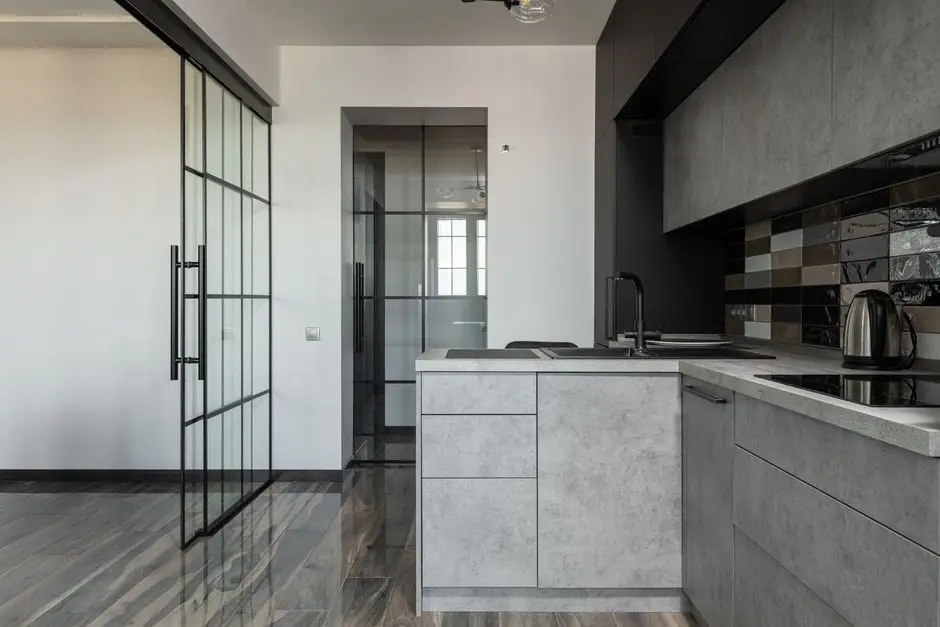 A black-framed glass partition door leading into a closed kitchen with a grey island